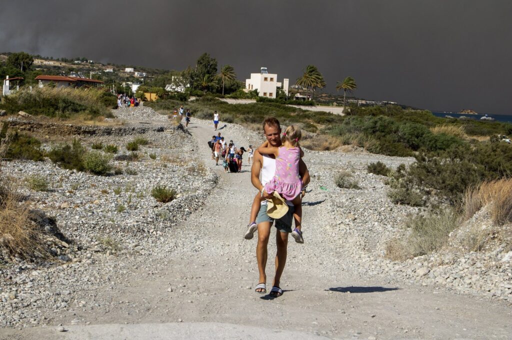 A man carries a child as they leave an area where a forest fire burns, Rhodes, Greece, July 22, 2023. (AP Photo)