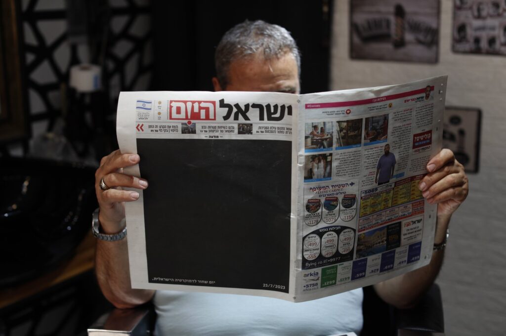 An Israeli hairdresser reads 'Israel Hayom' (Israel Today) with a blacked out front page and headline reading in Hebrew 'Black Day for Israeli Democracy,' Jerusalem, July 25, 2023. (EPA Photo)