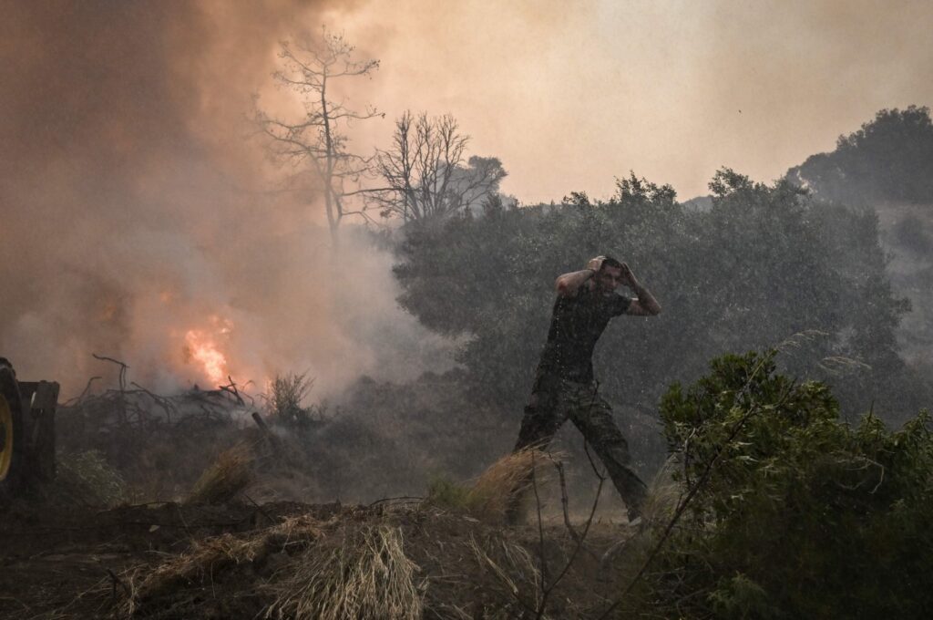 A man reacts as a helicopter sprays water at a fire on the island of Rhodes, Greece, July 25, 2023. (AFP Photo)