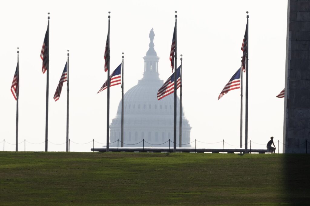 A visitor pauses at the base of the Washington Monument beneath U.S. national flags, with the U.S. Capitol seen in the background, in Washington, D.C., July 28, 2023. (EPA Photo)