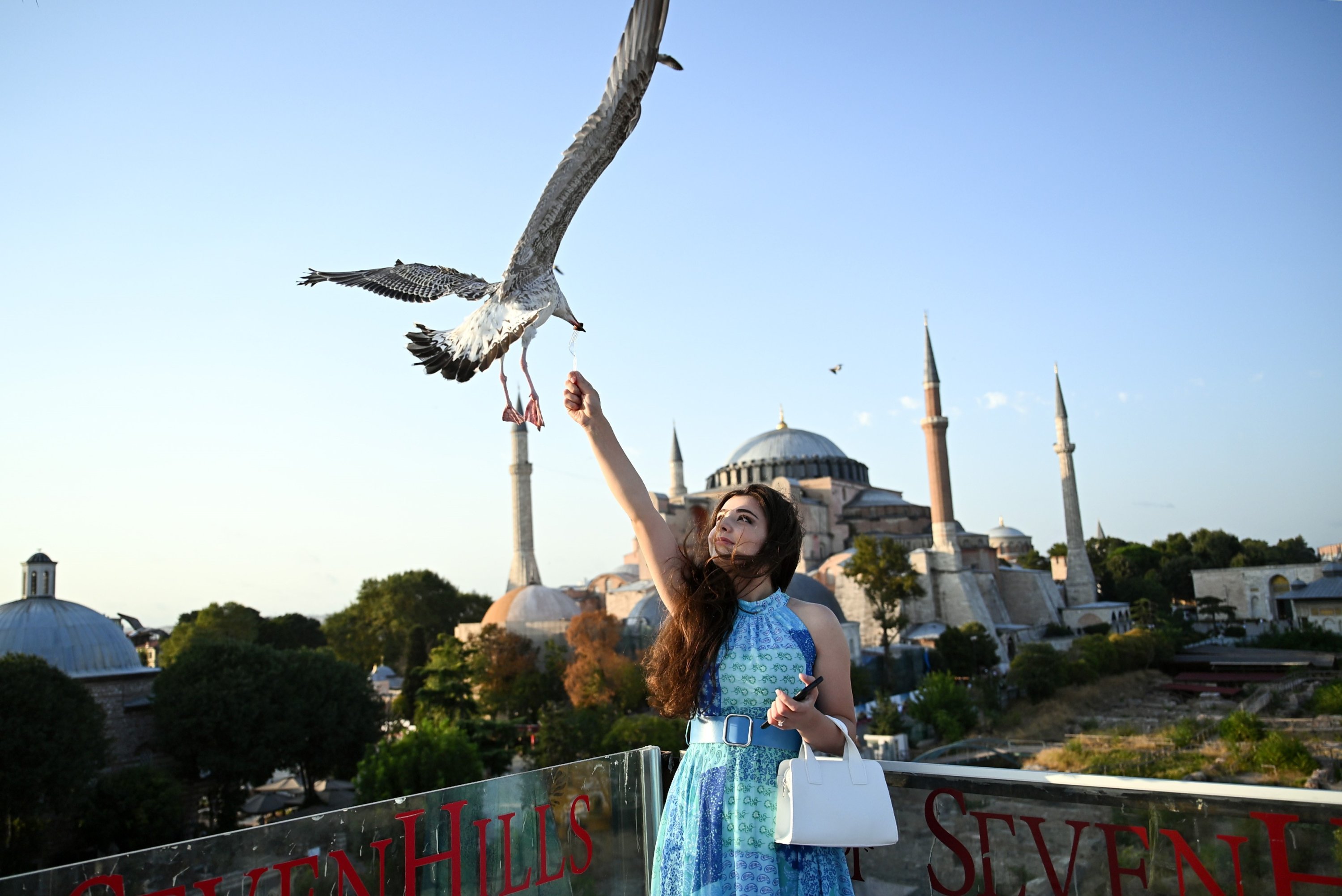 288314 A tourist poses while feeding a seagull in front of the Hagia Sophia Grand Mosque, Istanbul, Türkiye, Aug. 21, 2023. (IHA Photo)