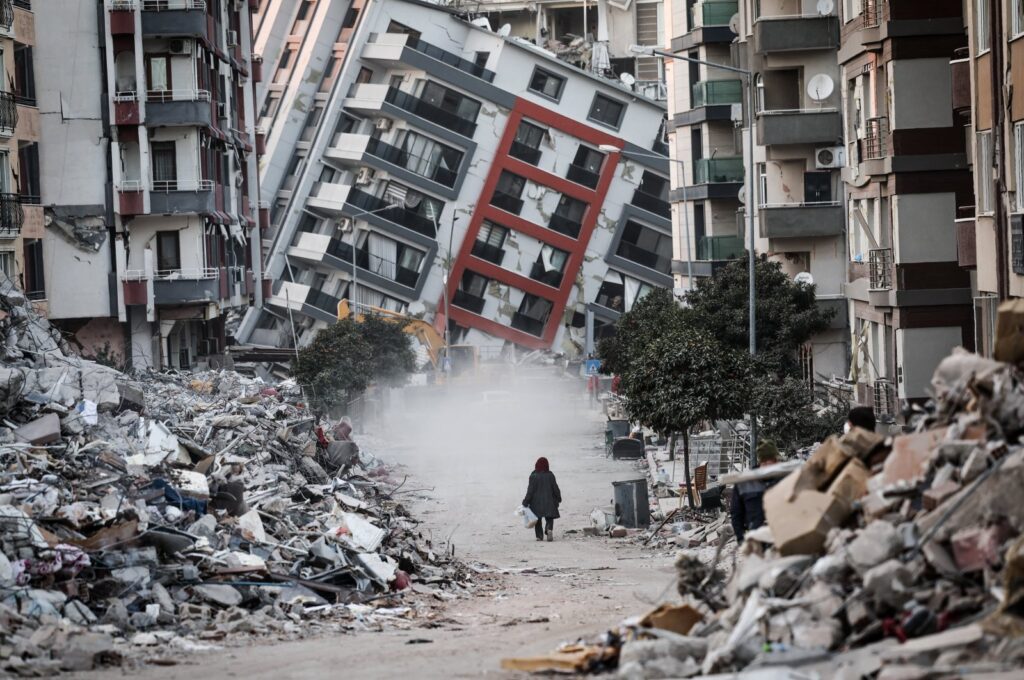 A woman walks in front of a collapsed building while demolition teams work after a powerful earthquake in Hatay, southeastern Türkiye, Feb. 17, 2023. (EPA Photo)