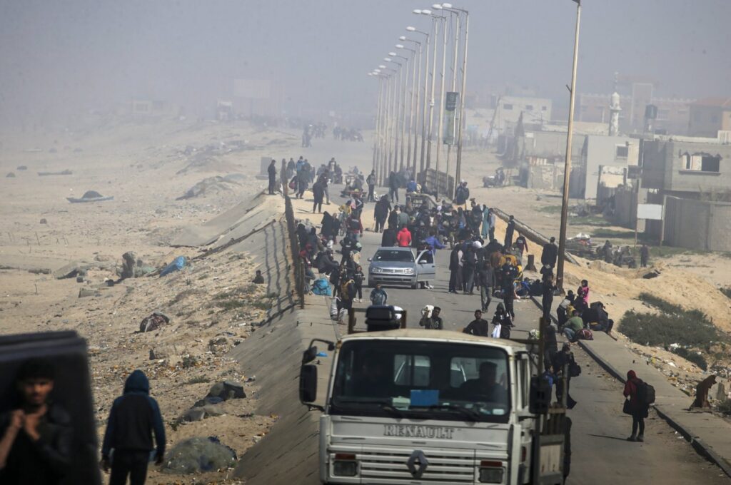 Dust and smoke from airstrikes engulf Palestinians walking along Al Rashid road after crossing from the northern Gaza Strip into the south of Gaza City, Feb. 25, 2024. (EPA Photo)