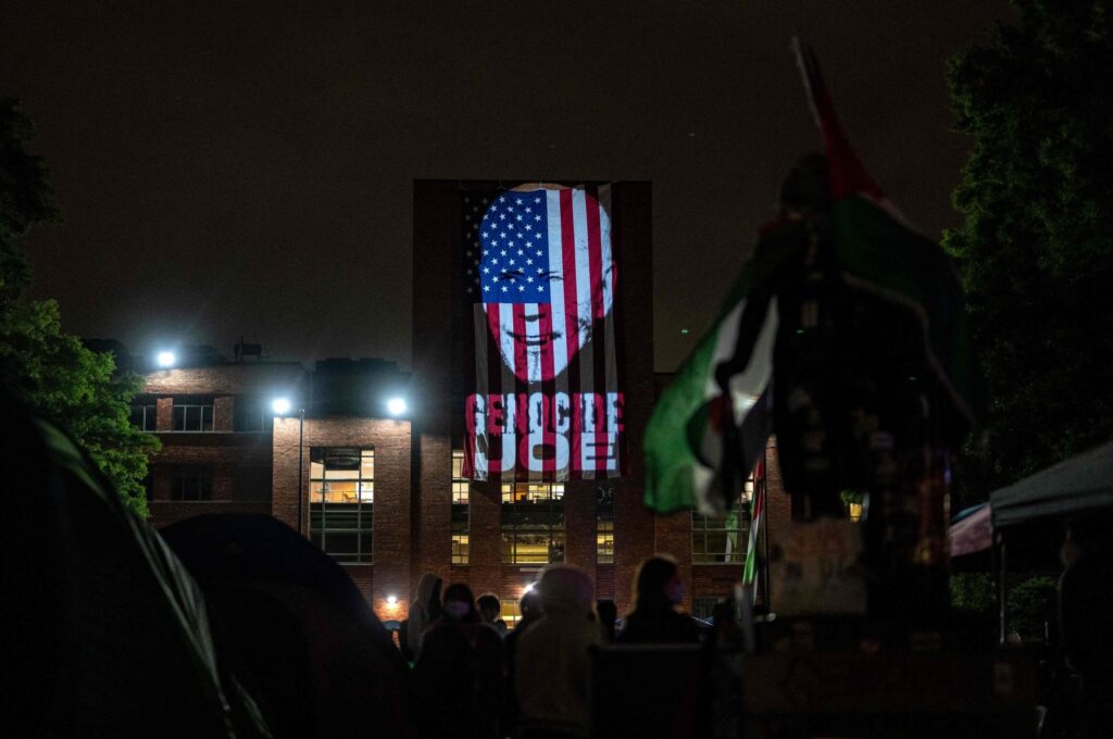 An image of President Joe Biden with the words "Genocide Joe" is projected on an American flag that hangs from GWU Law School's Lisner Hall at an encampment at University Yard at George Washington University on May 3, 2024 in Washington, D.C. (Getty Images via AFP)