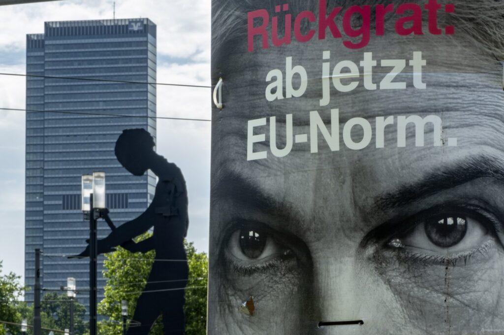 An election poster of Germany's Free Democratic Party's top candidate, Marie-Agnes Strack-Zimmermann fixed on a pole reads "spine: from now on EU norm" with "the hammering man", a statue by U.S. artist Jonathan Borofsky, is seen in the background, Frankfurt, Germany, June 5, 2024. (AP Photo)