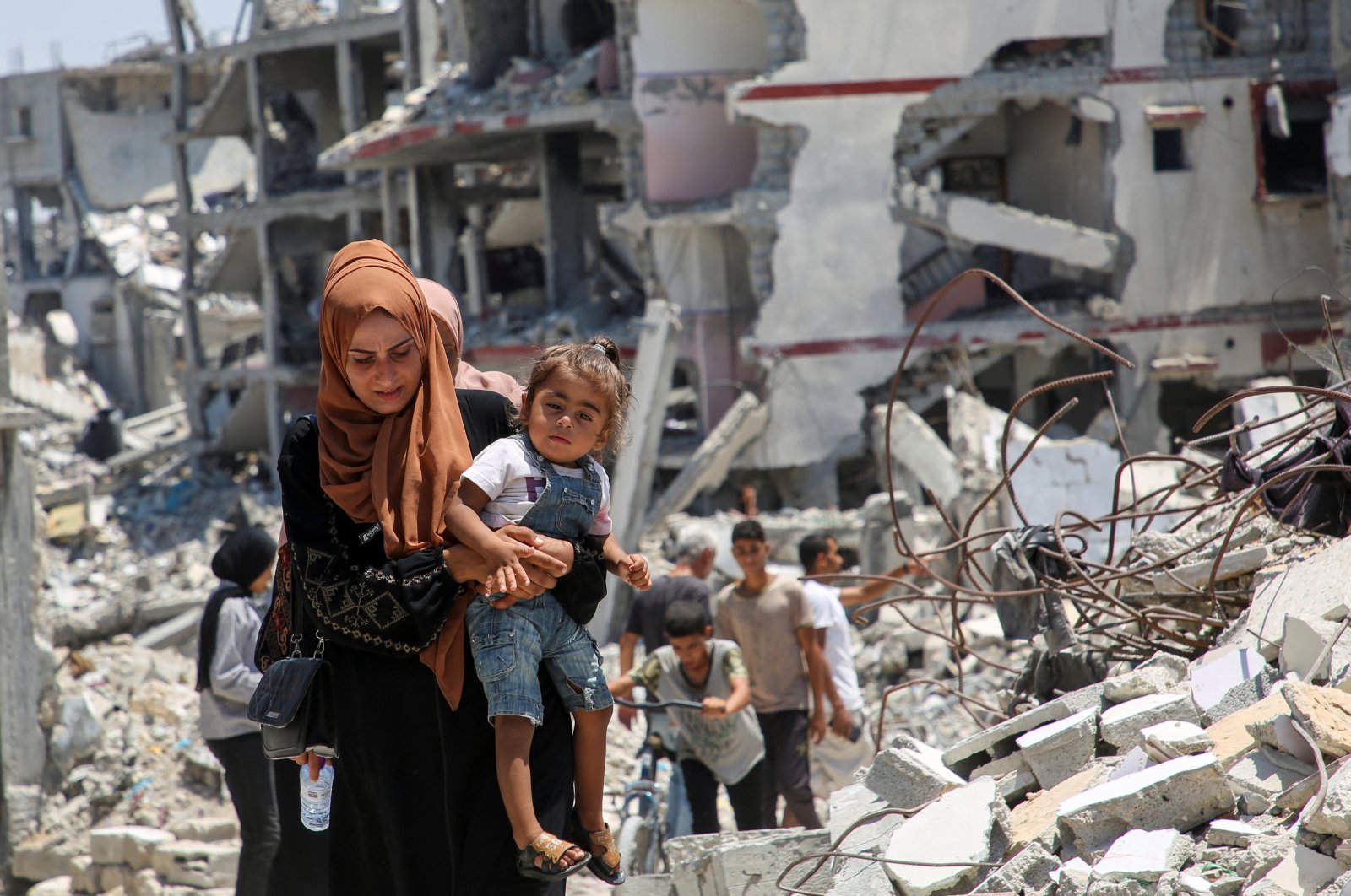 A Palestinian woman holds her daughter as she walks past the rubble of houses destroyed during the Israeli military offensive, Khan Younis, Gaza Strip, Palestine, July 10, 2024. (Reuters Photo)