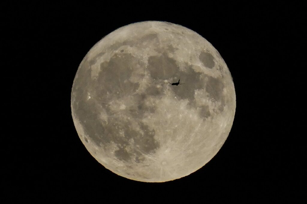 A plane passes in front of a full moon, Chicago, U.S., Aug. 30, 2023. (AP Photo)