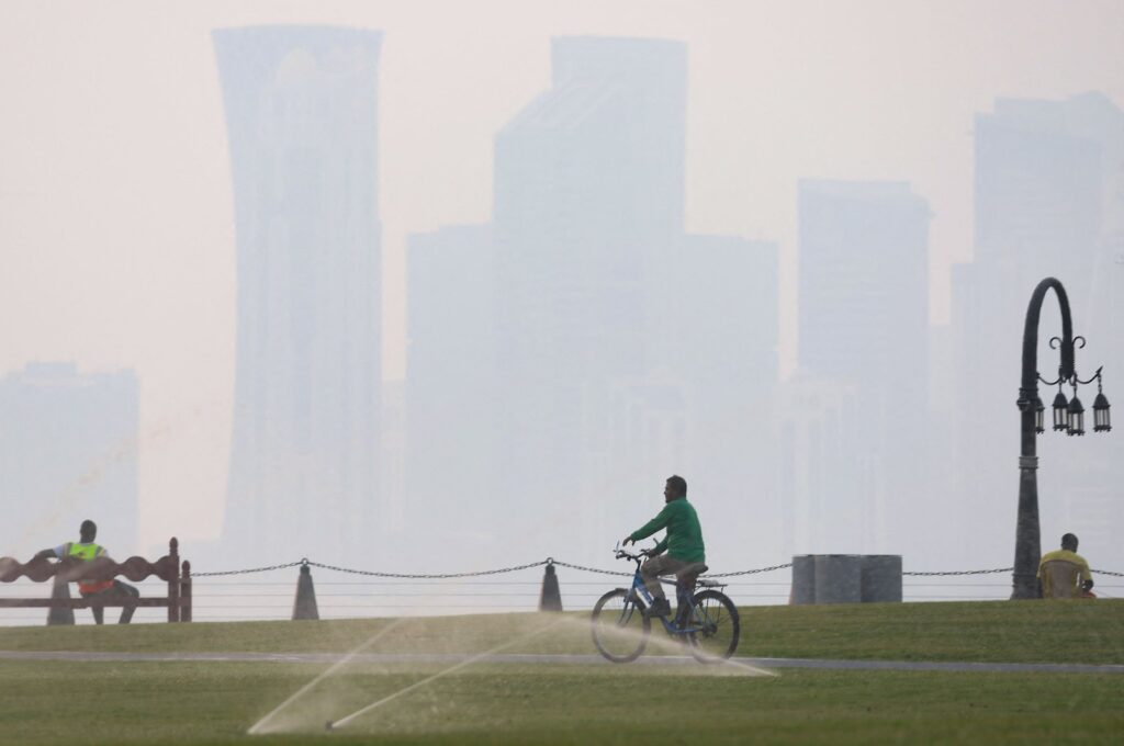 A man rides his bicycle as others sit on benches on a hot and humid summer day, in the West Bay district of Doha, Qatar, July 10, 2024. (AFP Photo)