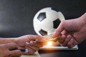 The photo shows two people exchanging money in front of a football and a tablet. (Getty Images Photo)