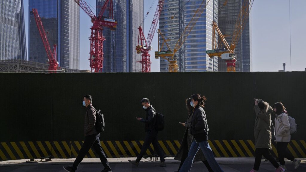 People wearing face masks walk by construction cranes near office buildings in the central business district, Beijing, China, March 15, 2023. (AP Photo)
