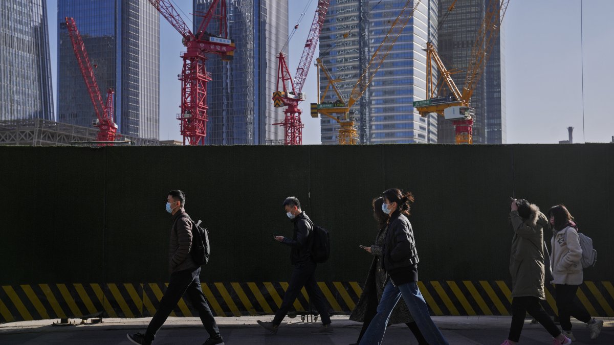 People wearing face masks walk by construction cranes near office buildings in the central business district, Beijing, China, March 15, 2023. (AP Photo)