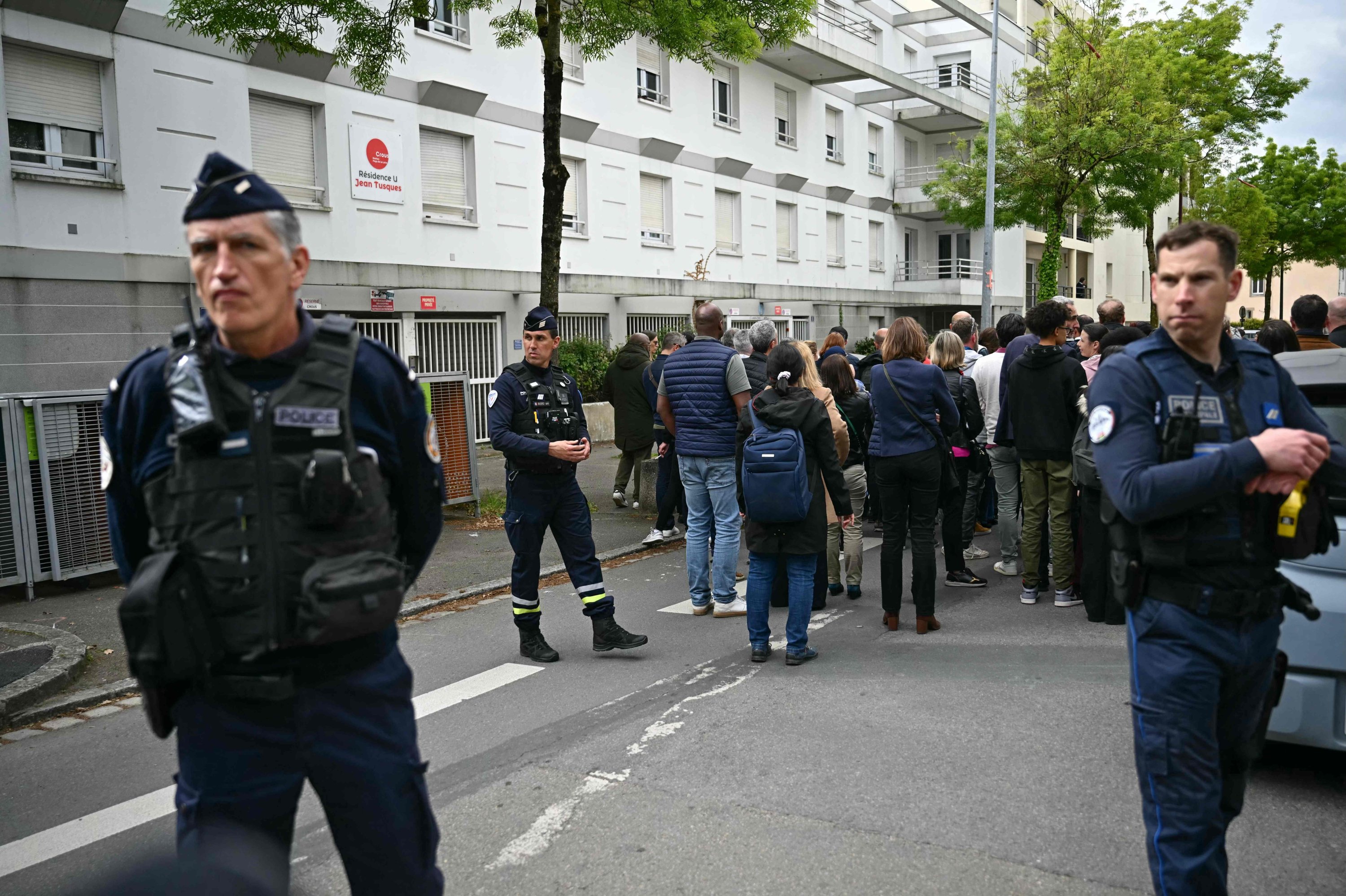 379332 A French police officer and a police municipal officer secure the school as parents wait students evacuate the high school Notre-Dame de Toutes-Aides after a knife attack, in Nantes, western France, on April 24, 2025. (AFP Photo)