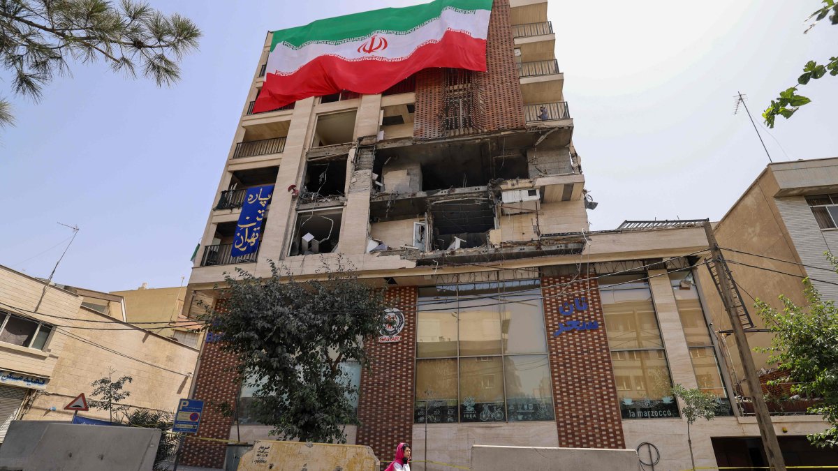 A woman walks past a residential building that was hit in an Israeli strike covered with a big Iranian flag, in Tehran, Iran, June 25, 2025. (AFP Photo)