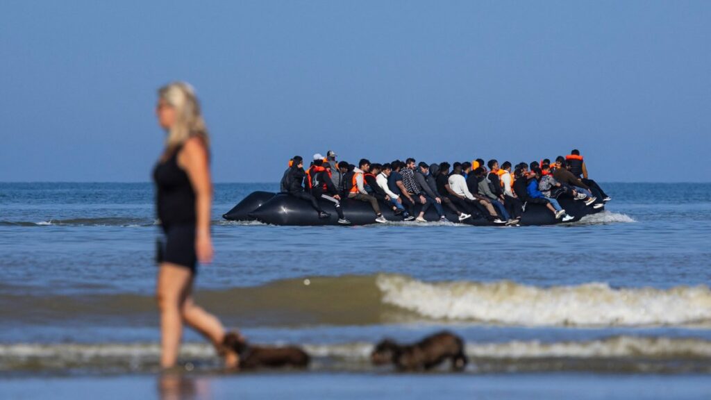 A tourist walks her dogs as migrants board a smuggler's boat in an attempt to cross the English Channel off the beach of Hardelot in Neufchatel-Hardelot, northern France, June 30, 2025. (AFP Photo)