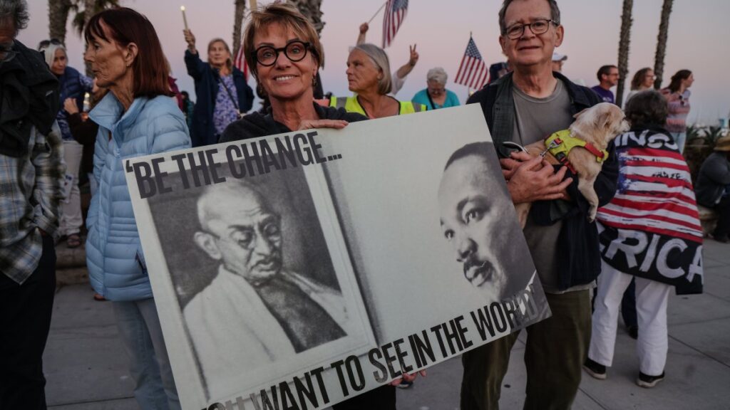 A protesting woman holds a sign that says "Be the Change You want to see in the world" with photos of Gandhi and Martin Luther King Jr. on the poster, in Santa Barbara, California, U.S., July 17, 2025. (Reuters Photo)